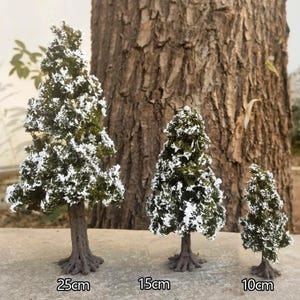 Puede incluir: Tres árboles artificiales en miniatura de hoja perenne con acentos de nieve. El árbol más grande mide 25 cm de altura, el árbol del medio mide 15 cm de altura y el árbol más pequeño mide 10 cm de altura. Los árboles tienen troncos marrones y follaje verde.