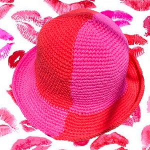 Puede incluir: Un sombrero de cubo de crochet rosa y rojo con un ala ancha. El sombrero está hecho de un hilo suave y texturizado y tiene un diseño simple y clásico.
