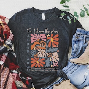 May include: A dark gray t-shirt with a floral design and the text "For I know the plans I have for you" and "Jeremiah 29:11 Plans to prosper you and not to harm you, plans to give you hope and a future".