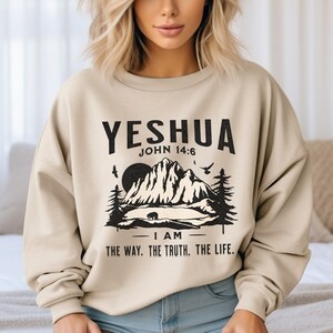 May include: A beige sweatshirt with a black graphic print of a mountain scene and the text "YESHUA JOHN 14:6 I AM THE WAY. THE TRUTH. THE LIFE."