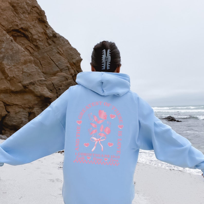 May include: A light blue hoodie with a pink graphic on the back that says "And the greatest of these is love" with a rose and hearts.