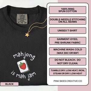 May include: Black unisex t-shirt with the phrase "mahjong is mah jam" and a strawberry-themed mahjong tile design. The shirt is made of 100% ring-spun cotton and features double-needle stitching. A gold star pendant hangs from a gold chain.