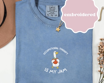 May include: Blue jean Comfort Colors t-shirt with the text "Occupational Therapy Is My Jam" and a cartoon goose holding a strawberry. The shirt is embroidered and has a tag that says XL-TG-EG.