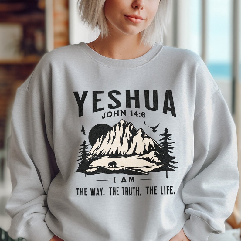 May include: A light grey sweatshirt with a black graphic design featuring a mountain range, a bear, and the text "YESHUA JOHN 14:6 -I AM THE WAY. THE TRUTH. THE LIFE."