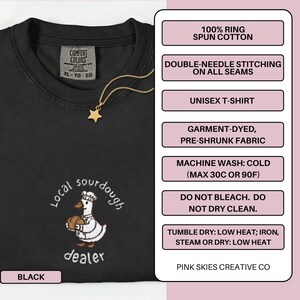 Puede incluir: Camiseta unisex negra con un dise&ntilde;o bordado en blanco de un pato chef sosteniendo pan, y las palabras "Local sourdough dealer". La camiseta tiene un collar de estrella dorada. Hecha de algod&oacute;n 100% hilado en anillo.