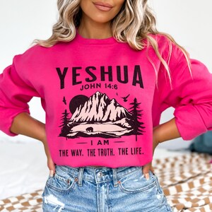 May include: Pink sweatshirt featuring a mountain scene and the text "YESHUA JOHN 14:6 I AM THE WAY. THE TRUTH. THE LIFE."