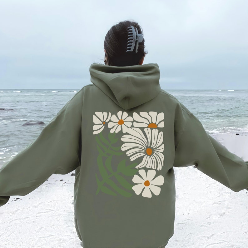 Puede incluir: Una sudadera con capucha verde con un estampado de margaritas blancas en la espalda.