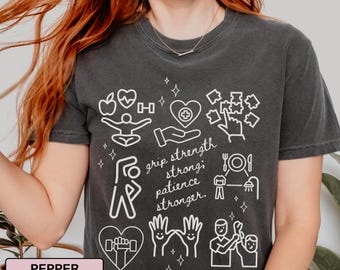 Op de afbeelding: Donkergrijs t-shirt met witte grafische iconen en tekst. Het ontwerp bevat een hart, appel, halter en handen. Tekst luidt "grip strength, strong, patience, stronger."