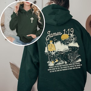 May include: A dark green hoodie with a cross on the front and a graphic on the back. The graphic features a person hiking in a forest with a river and the text "James 1:12". The text below the graphic reads "Blessed is the one who perseveres under trial because, having stood the test, that person will receive the crown of life that the Lord has promised to those who love him."