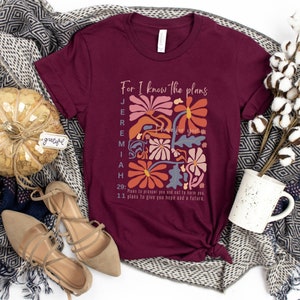 May include: A maroon t-shirt with a floral design and the text "For I know the plans I have for you" and "Jeremiah 29:11 Plans to prosper you and not to harm you, plans to give you hope and a future."