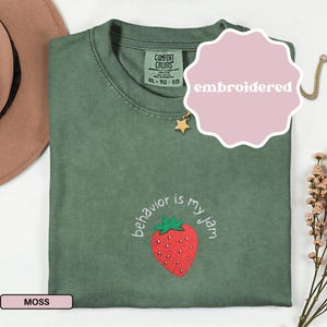 Peut inclure: T-shirt vert mousse avec une fraise brod&eacute;e et l'inscription "behavior is my jam". Le t-shirt a un col rond et des manches courtes. L'&eacute;tiquette indique "Comfort Colors" et XL-TG-EG.