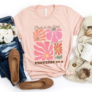 Peut inclure: Un t-shirt rose avec un motif floral et le texte "Trust in the Lord with all your heart Proverbs 3:5-6".