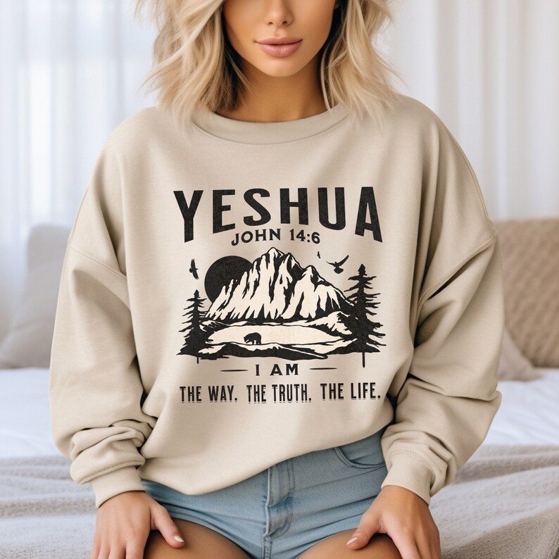 May include: A beige sweatshirt with a black graphic print of a mountain scene and the text "YESHUA JOHN 14:6 I AM THE WAY. THE TRUTH. THE LIFE."