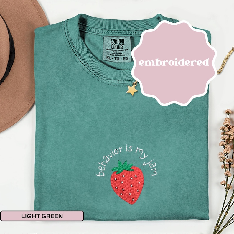 Peut inclure: Un t-shirt vert clair avec le texte "behavior is my jam" brod&eacute; sous une fraise rouge. Le t-shirt est &eacute;tiquet&eacute; "Comfort Colors" et est de taille XL-TG-EG. Un autocollant rose avec le mot "embroidered" est sur le t-shirt.