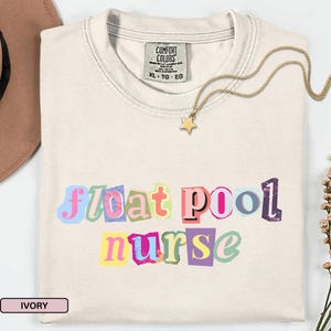 Op de afbeelding: Ivoor kleurig t-shirt met de woorden "float pool nurse" in kleurrijke, uitgesneden letters. Een gouden ster hanger ketting rust op het shirt. Het shirt heeft een Comfort Colors label, maat XL-TG-EG.
