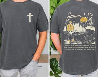 May include: A dark grey t-shirt with a cross on the front and a graphic of a person hiking in a forest with the text "James 1:12" on the back. The text below the graphic reads "Blessed is the one who perseveres under trial because, having stood the test, that person will receive the crown of life that the Lord has promised to those who love him."