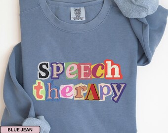 Puede incluir: Una sudadera azul vaquero con las palabras "Speech Therapy" en un estilo recortado y colorido. La sudadera tiene cuello redondo y mangas largas. Una scrunchie a juego descansa sobre el hombro.