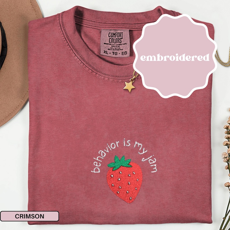 Peut inclure: T-shirt de couleur cramoisie avec la phrase brod&eacute;e "behavior is my jam" et une fraise. Le t-shirt est de la marque Comfort Colors, taille XL-TG-EG. Un pendentif &eacute;toile dor&eacute; est suspendu pr&egrave;s de l'encolure.