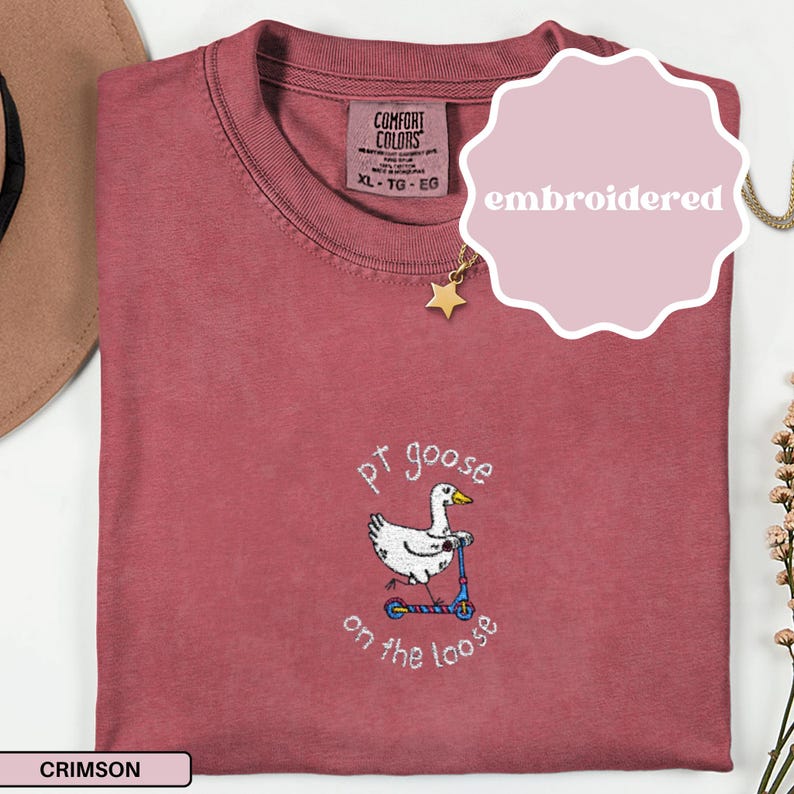May include: Crimson-colored Comfort Colors t-shirt with an embroidered design. The design features a goose riding a scooter with the text "pt goose on the loose". The shirt has a crew neck and a tag that says XL-TG-EG.