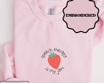 Puede incluir: Sudadera rosa claro con la frase "speech therapy is my jam" y un diseño de fresa roja. La palabra "EMBROIDERED" está en un círculo rosa con contorno negro. Las palabras "LIGHT PINK" están en un rectángulo blanco.