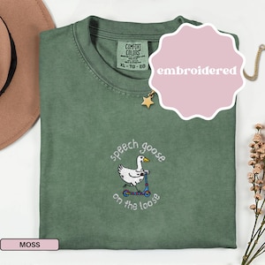 May include: Moss green t-shirt with an embroidered design of a goose on a scooter, with the text "speech goose on the loose". The shirt has a crew neck and short sleeves. The tag reads "Comfort Colors".