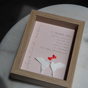 May include: A framed pink and white paper art piece with a message that reads "I choose you and I'll choose you over and over without pause without a doubt in a heartbeat I'll keep choosing you". The art piece features two white origami birds with red hearts above them.