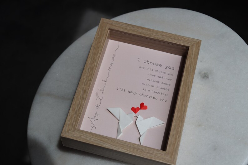 May include: A framed pink and white paper art piece with a message that reads "I choose you and I'll choose you over and over without pause without a doubt in a heartbeat I'll keep choosing you". The art piece features two white origami birds with red hearts above them.