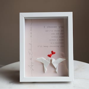 May include: White frame with a pink background and a handwritten message that reads "Amy & Edmund 08.08.2020" and "I choose you and I'll choose you over and over without pause without a doubt in a heartbeat I'll keep choosing you". Two white origami doves are in the center of the frame with three red paper hearts above them.