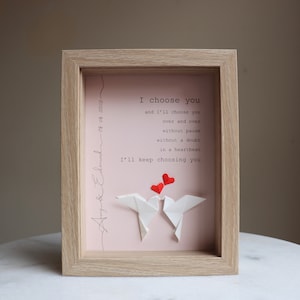 May include: A framed pink and white print with the text "I choose you and I'll choose you over and over without pause without a doubt in a heartbeat I'll keep choosing you". Two white origami doves are holding red hearts above them. The frame is light brown wood.