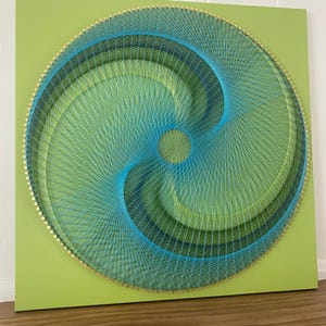May include: A green square canvas with a circular string art design. The design features a swirling pattern of blue and green thread.