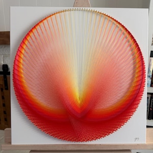 Könnte beinhalten: Eine quadratische weiße Leinwand mit einem kreisförmigen Fadenkunst-Design. Das Kunstwerk verwendet dünne Fäden in einem Farbverlauf von Gelb, Orange und Rot, die von der Mitte zum Rand strahlen und ein lebendiges, symmetrisches Muster bilden.