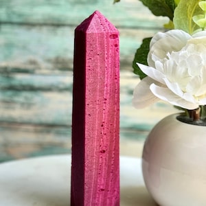 May include: A tall, pink, rectangular obelisk with a pointed top. The obelisk is made of a textured material and has a slightly rough surface.