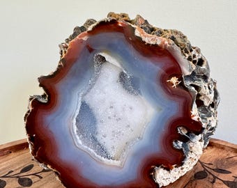 May include: A large, natural agate geode with a red, white, and blue banded pattern. The geode is cut in half, revealing a hollow center filled with sparkling crystals.