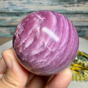 Peut inclure: Une sphère de pierre polie, rose avec des veines blanches, tenue dans une main. La surface polie présente un motif tourbillonnant et texturé. L'arrière-plan est flou, mettant l'accent sur l'orbite.