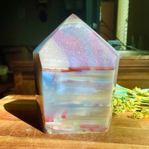 May include: A large, clear, faceted crystal with red, white, and blue banding. The crystal is shaped like a pyramid and has a smooth, polished surface.