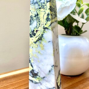 May include: A white, green, and black obelisk crystal point. The crystal has a unique marbled pattern.