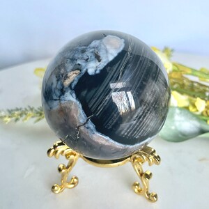 May include: A black and white agate sphere on a gold metal stand. The sphere has a swirling pattern of black and white.