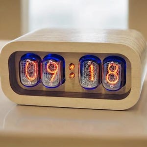 May include: A wooden clock with a retro design features four Nixie tubes displaying the time 09:18. The clock has a light wood finish and a rounded rectangular shape.