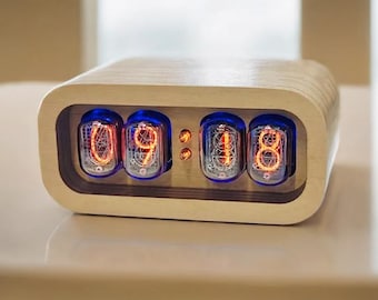 May include: A wooden clock with a retro design features four Nixie tubes displaying the time 09:18. The clock has a light wood finish and a rounded rectangular shape.