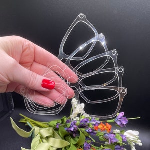 May include: A set of six clear plastic stencils in the shape of a butterfly. The stencils are stacked on top of each other and are being held in a hand.