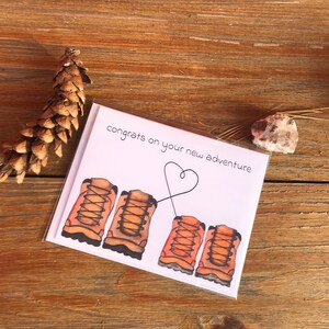 May include: A white card with the text "congrats on your new adventure" and a drawing of four brown hiking boots with laces tied together in a heart shape.