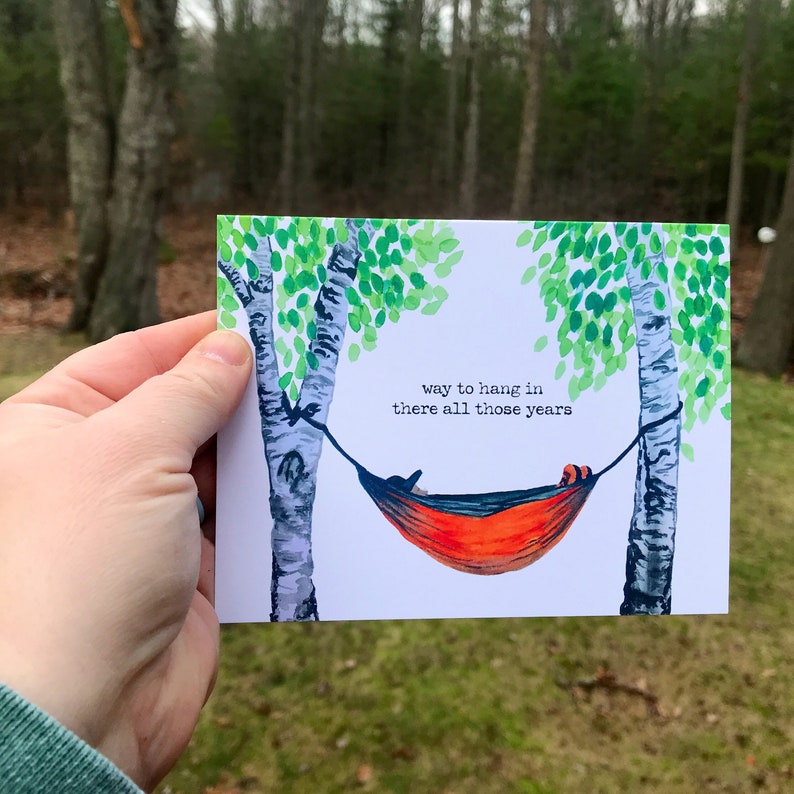 May include: A greeting card with a watercolor illustration of a hammock hanging between two birch trees. The text on the card reads "way to hang in there all those years".