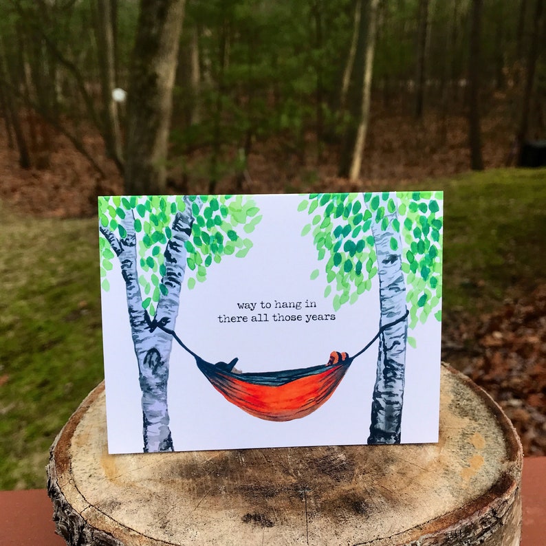 May include: A greeting card with a watercolor illustration of a red hammock hanging between two birch trees. The text on the card reads "way to hang in there all those years".