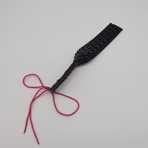 Pode incluir: Uma pulseira de borracha preta com um padrão de banda de rodagem de pneu e laços de corda rosa.