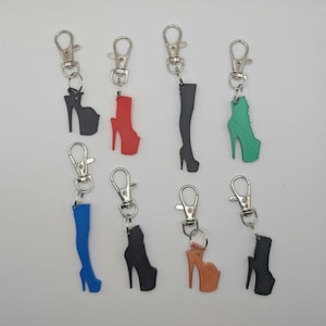 Könnte beinhalten: Acht verschiedene farbige Schlüsselanhänger mit verschiedenen Designs von High-Heel-Schuhen. Die Schlüsselanhänger sind aus Metall und Kunststoff und haben einen silbernen Federclip.