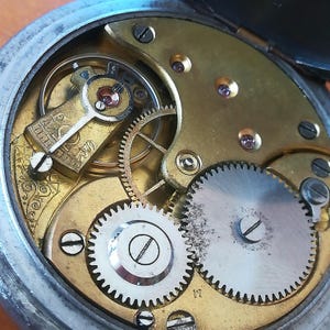 May include: Close-up view of the inner workings of a vintage pocket watch. The intricate gears and mechanisms are visible, showcasing the craftsmanship of the watchmaker. The watch face is not visible in this image.
