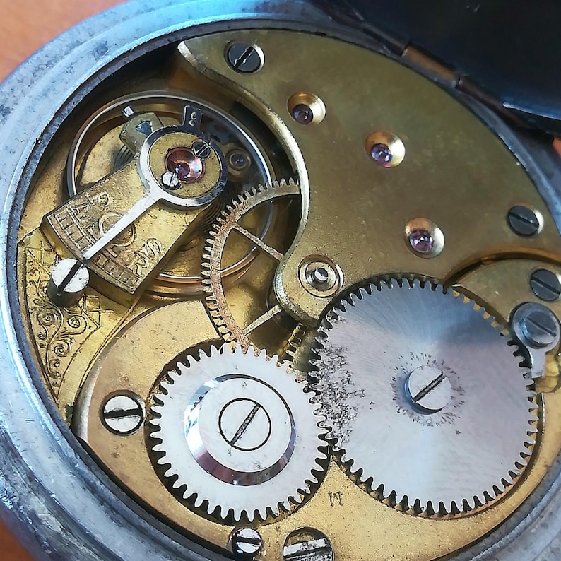 May include: Close-up view of the inner workings of a vintage pocket watch. The intricate gears and mechanisms are visible, showcasing the craftsmanship of the watchmaker. The watch face is not visible in this image.