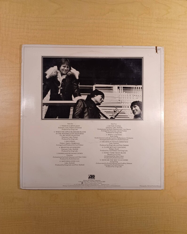 Puede incluir: Contraportada de un &aacute;lbum de vinilo con una foto en blanco y negro de tres hombres. El &aacute;lbum se titula "Emerson, Lake & Palmer". La lista de canciones del &aacute;lbum est&aacute; impresa en la contraportada.