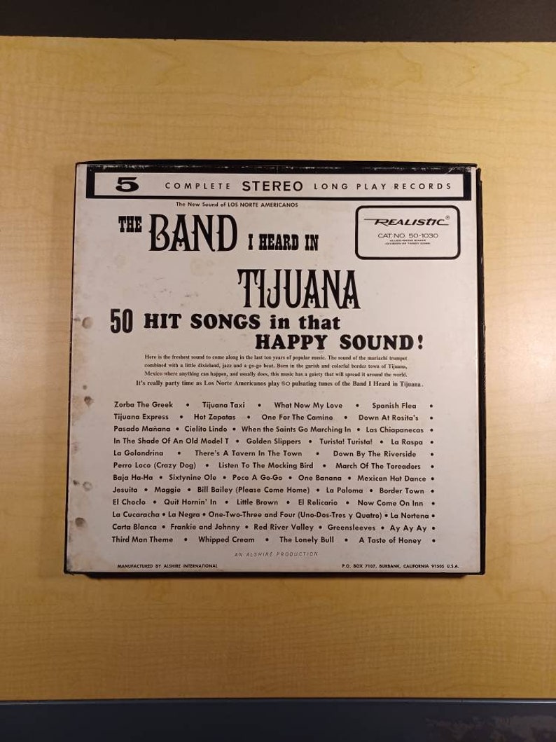 May include: A black and white record album cover with the title "The Band I Heard In Tijuana" and a list of 50 hit songs in that happy sound. The album cover features a red and white "Realistic" logo with the catalog number "50-1030".