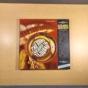 May include: A Realistic 50 Big Hits record album featuring The Band Heard in Tijuana. The album cover features a gold trumpet with the band's name in a circular design. The album is part of the Audiophile Series and has a 33 1/3 RPM speed.